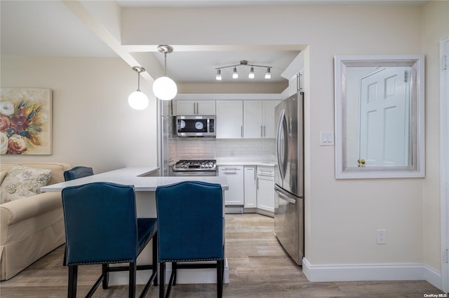 kitchen with hanging light fixtures, light wood-type flooring, a kitchen bar, white cabinetry, and stainless steel appliances