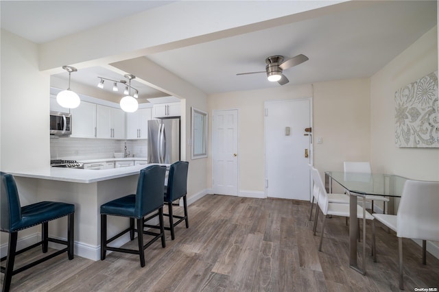 kitchen featuring kitchen peninsula, tasteful backsplash, stainless steel appliances, white cabinets, and hardwood / wood-style floors