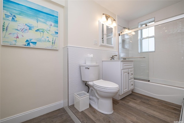 full bathroom with hardwood / wood-style floors, bath / shower combo with glass door, toilet, vanity, and tile walls