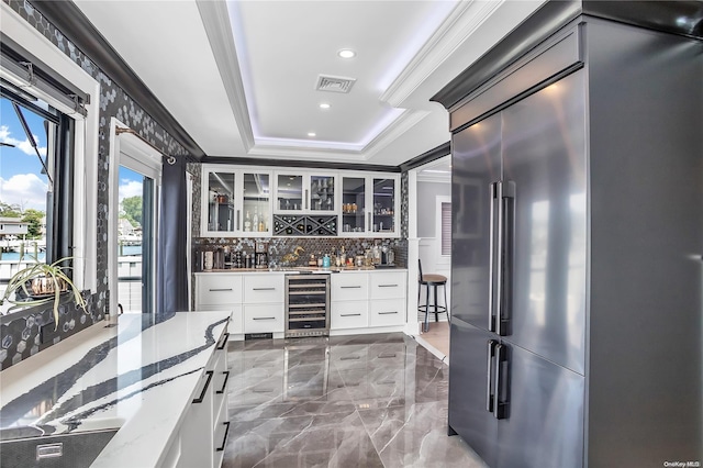 kitchen featuring tasteful backsplash, wine cooler, light stone counters, crown molding, and white cabinets