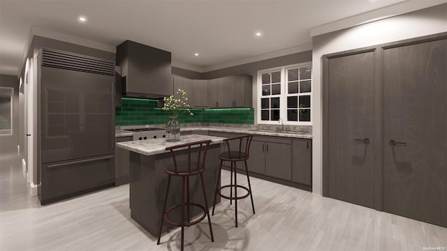 kitchen with backsplash, wall chimney exhaust hood, sink, a center island, and built in fridge