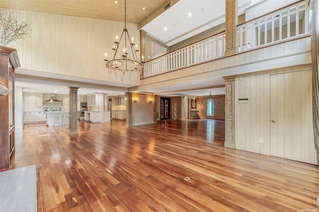 unfurnished living room with hardwood / wood-style flooring, a chandelier, high vaulted ceiling, and decorative columns