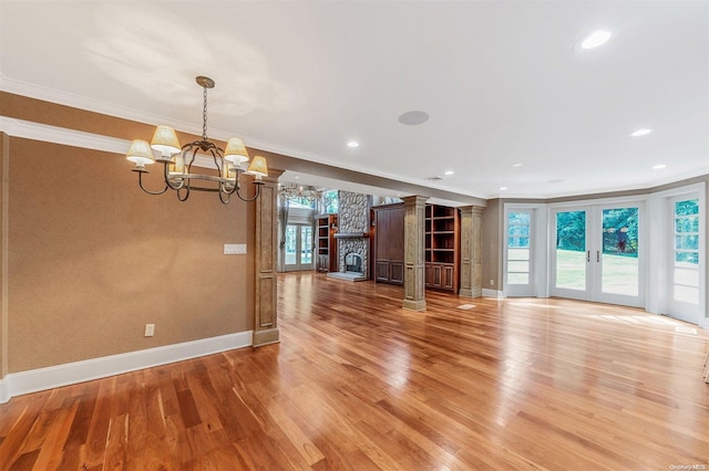 unfurnished living room with french doors, decorative columns, crown molding, wood-type flooring, and a notable chandelier