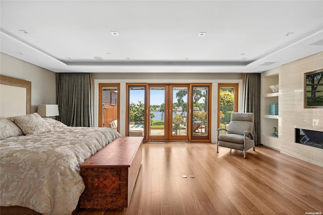 bedroom with a high end fireplace, access to outside, french doors, a tray ceiling, and light hardwood / wood-style floors