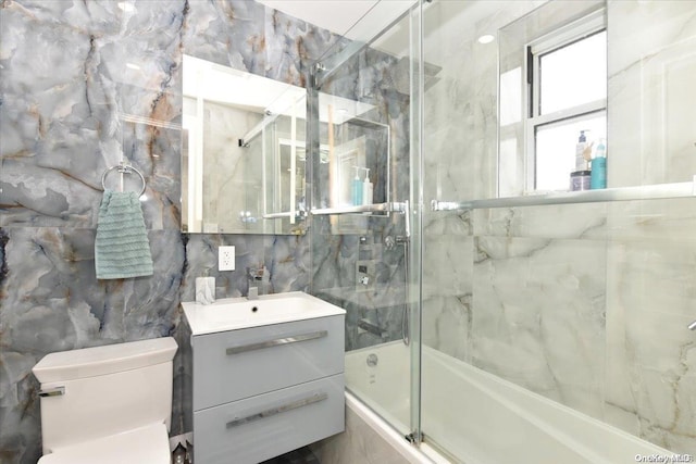 full bathroom with vanity, toilet, bath / shower combo with glass door, and tile walls