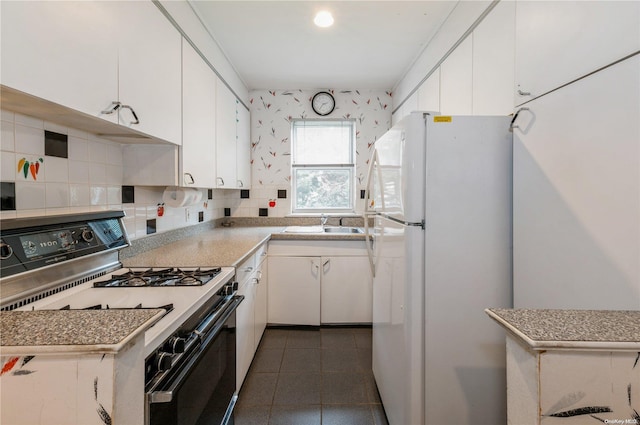 kitchen with tasteful backsplash, white cabinets, gas range oven, and white fridge