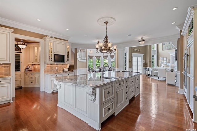 kitchen with sink, hanging light fixtures, backsplash, a kitchen island with sink, and hardwood / wood-style flooring