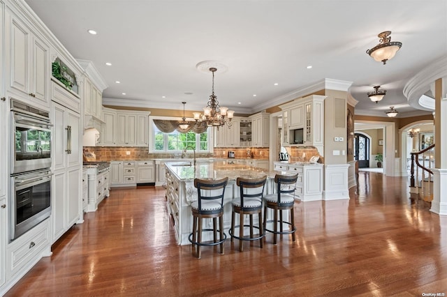 kitchen featuring tasteful backsplash, a kitchen breakfast bar, dark hardwood / wood-style flooring, pendant lighting, and a center island with sink