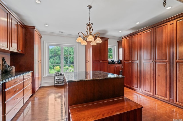 kitchen with dark stone countertops, a center island, decorative light fixtures, and ornamental molding