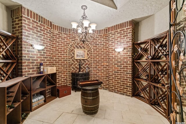 wine area featuring a chandelier, a textured ceiling, and brick wall