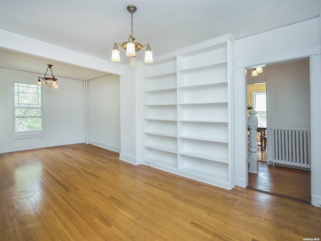 spare room with a chandelier, hardwood / wood-style flooring, built in features, and radiator