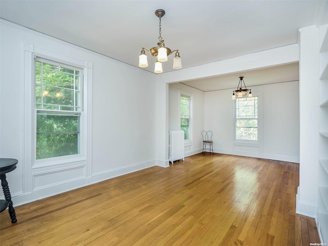 interior space featuring radiator heating unit, an inviting chandelier, a wealth of natural light, and wood-type flooring