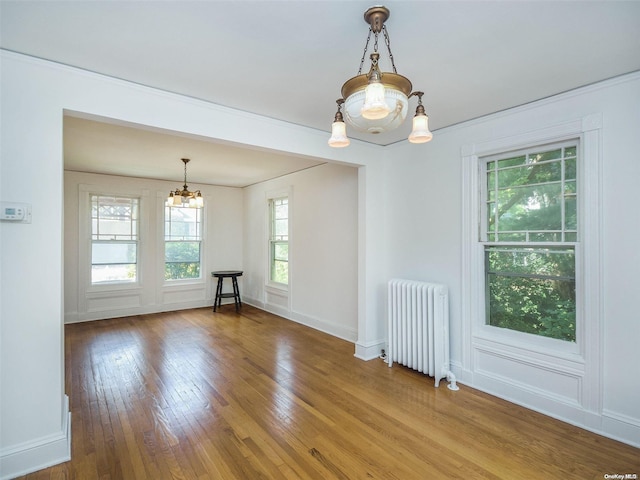 empty room with a chandelier, radiator heating unit, and hardwood / wood-style floors