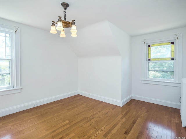 additional living space featuring dark hardwood / wood-style floors, vaulted ceiling, a wealth of natural light, and a chandelier