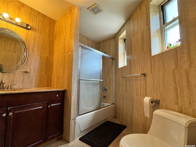 full bathroom with combined bath / shower with glass door, toilet, and tile walls