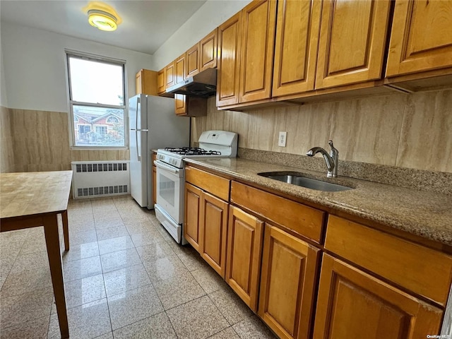 kitchen featuring white gas stove, light stone counters, radiator heating unit, and sink