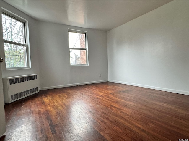 unfurnished room featuring dark hardwood / wood-style flooring, radiator heating unit, and a healthy amount of sunlight