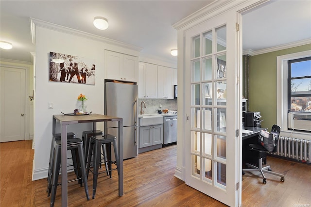 kitchen with tasteful backsplash, stainless steel appliances, crown molding, hardwood / wood-style flooring, and radiator heating unit