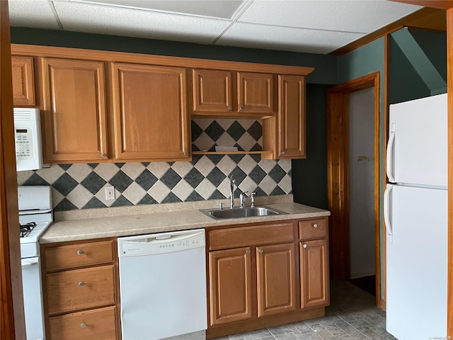 kitchen with a paneled ceiling, white appliances, sink, and tasteful backsplash