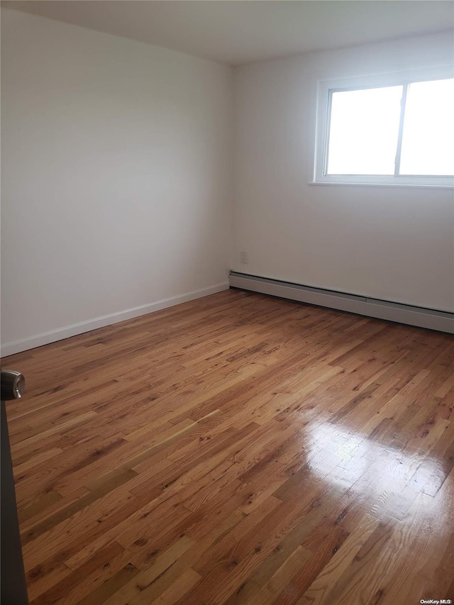 empty room featuring a baseboard heating unit and hardwood / wood-style flooring