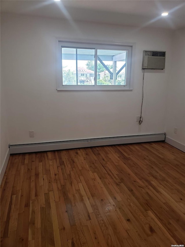 spare room featuring hardwood / wood-style flooring, an AC wall unit, and baseboard heating