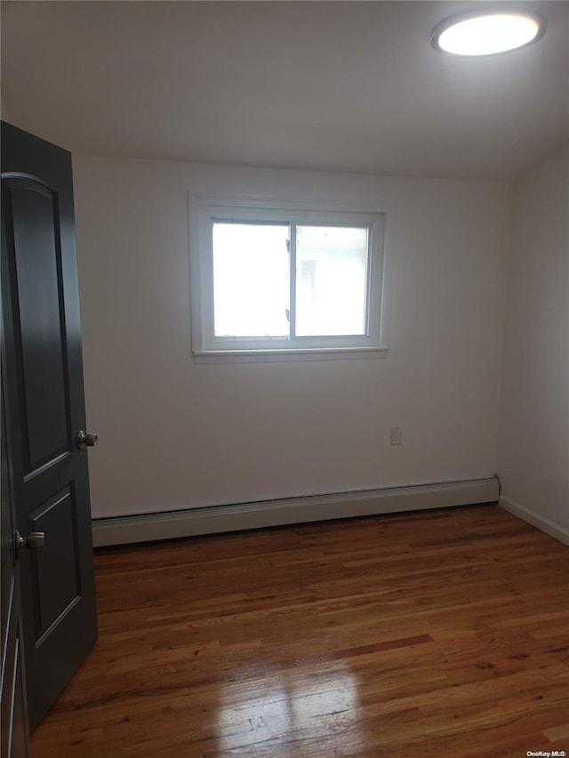 unfurnished room with dark hardwood / wood-style flooring and a baseboard heating unit