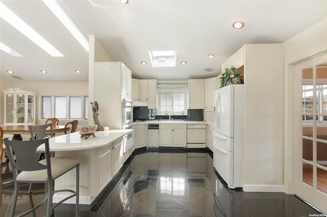 kitchen with plenty of natural light, white appliances, kitchen peninsula, and a skylight