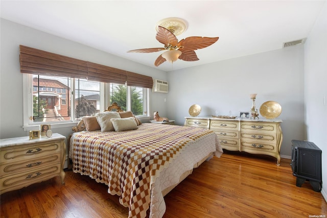 bedroom featuring a wall mounted AC, ceiling fan, and hardwood / wood-style flooring