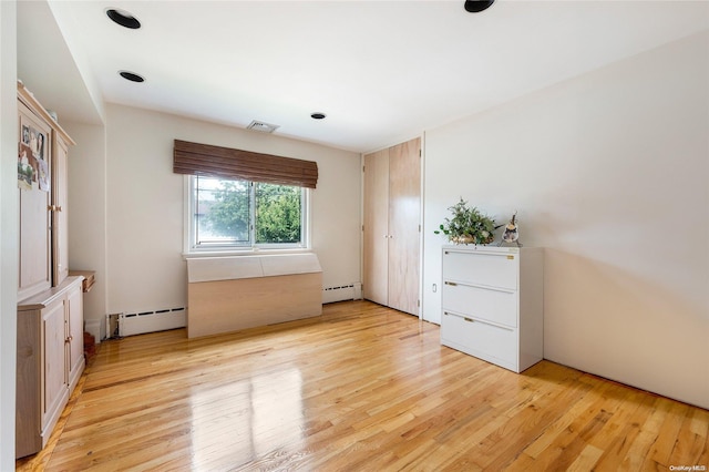 unfurnished bedroom featuring light wood-type flooring and a baseboard heating unit