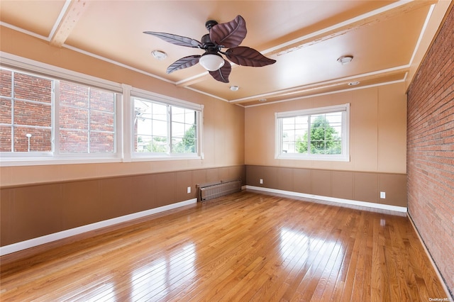 unfurnished room featuring beamed ceiling, light hardwood / wood-style floors, a healthy amount of sunlight, and brick wall