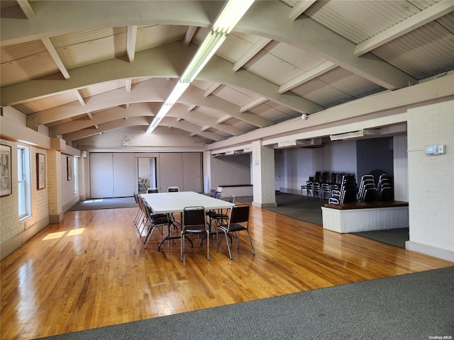 dining room with vaulted ceiling with beams, light hardwood / wood-style floors, and brick wall