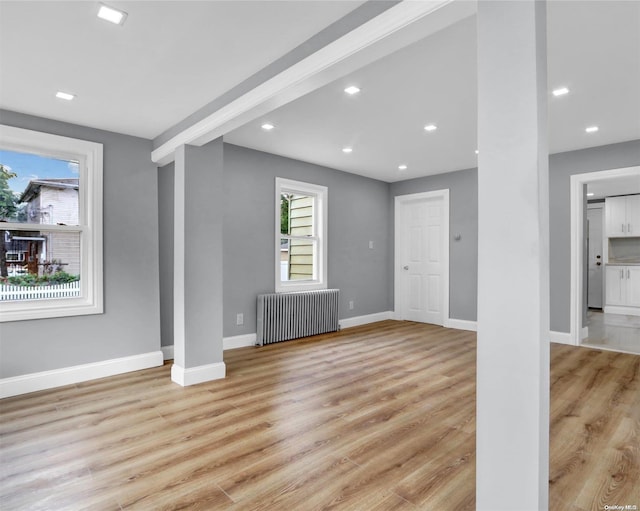 unfurnished living room featuring beamed ceiling, light hardwood / wood-style floors, and radiator