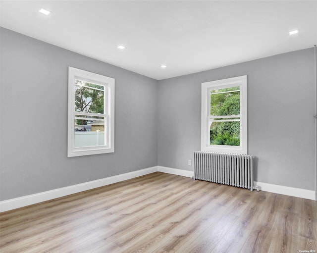 empty room featuring a wealth of natural light, light wood-type flooring, and radiator