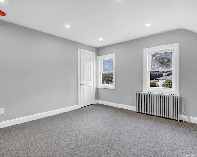 spare room featuring carpet flooring, radiator, and vaulted ceiling