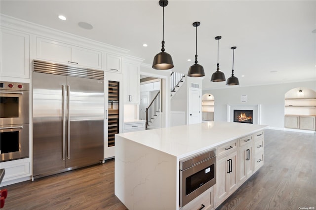 kitchen with pendant lighting, built in appliances, a center island, and white cabinetry