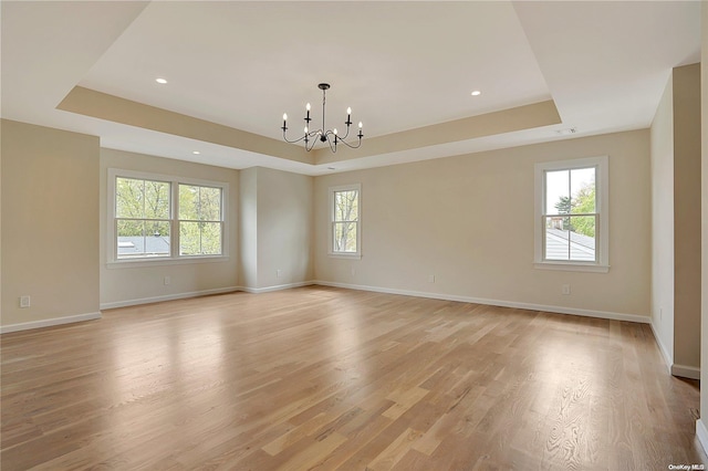 spare room with an inviting chandelier, a raised ceiling, and light hardwood / wood-style floors