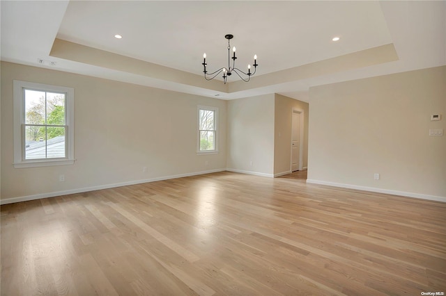 empty room with a notable chandelier, light hardwood / wood-style floors, and a tray ceiling