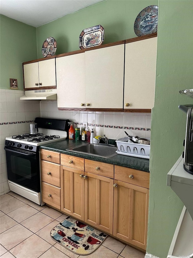 kitchen featuring backsplash, sink, light tile patterned floors, and white gas range oven