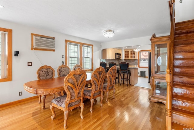 dining space featuring radiator heating unit, a textured ceiling, light hardwood / wood-style floors, and an AC wall unit