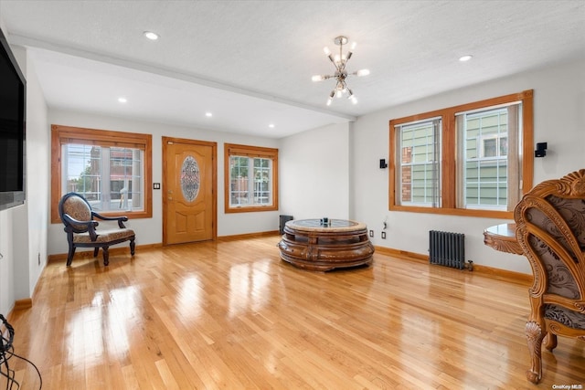 living area with radiator heating unit, light hardwood / wood-style floors, a textured ceiling, and an inviting chandelier