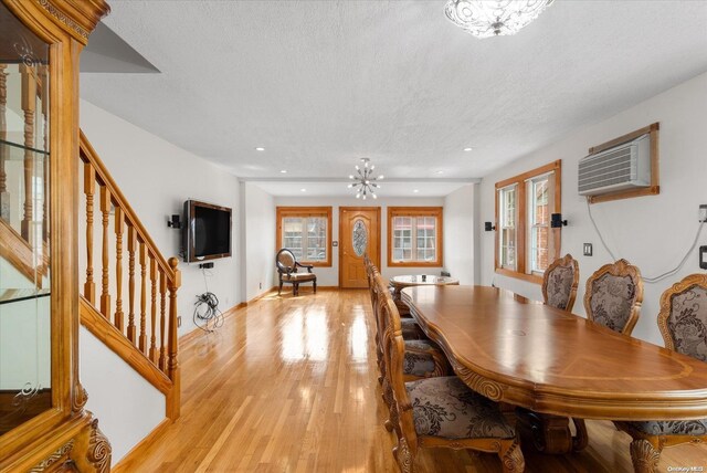 dining room featuring an AC wall unit, a textured ceiling, and light hardwood / wood-style flooring