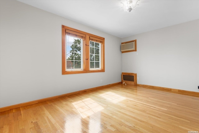 unfurnished room with light hardwood / wood-style floors, a wall unit AC, and heating unit