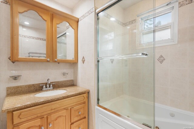 bathroom featuring backsplash, vanity, bath / shower combo with glass door, and tile walls