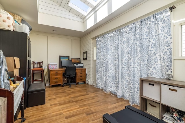 home office featuring light hardwood / wood-style floors, vaulted ceiling, and brick wall