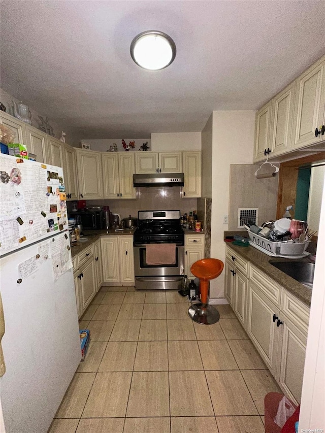 kitchen with white refrigerator, light tile patterned floors, tasteful backsplash, cream cabinetry, and gas stove