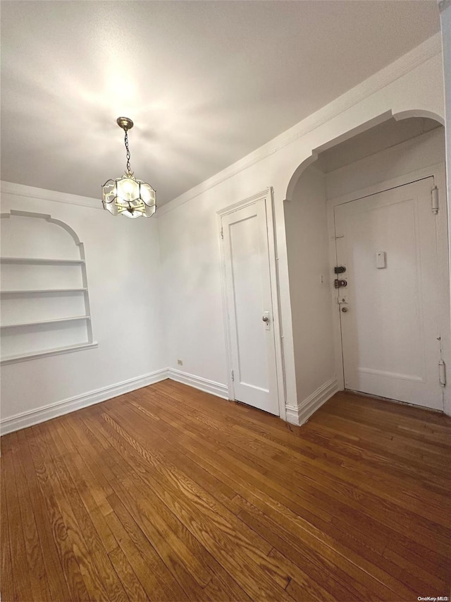 empty room with built in shelves, a notable chandelier, and hardwood / wood-style flooring