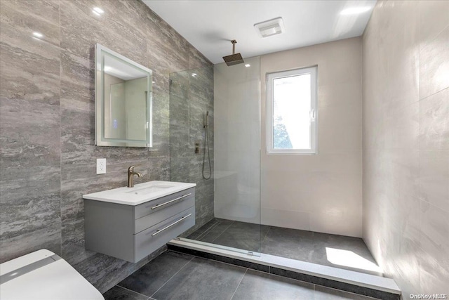 bathroom with a tile shower, tile patterned floors, vanity, and tile walls