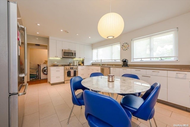 kitchen featuring hanging light fixtures, light tile patterned floors, white cabinetry, stainless steel appliances, and washing machine and clothes dryer