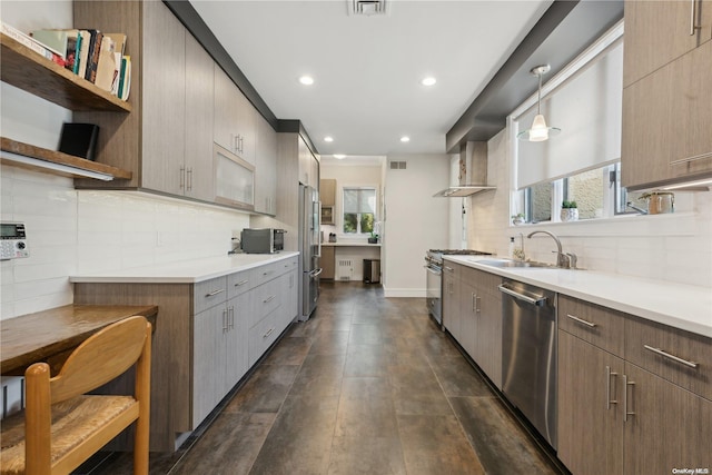 kitchen featuring sink, wall chimney range hood, pendant lighting, decorative backsplash, and appliances with stainless steel finishes