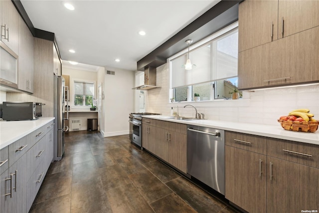 kitchen with appliances with stainless steel finishes, tasteful backsplash, wall chimney exhaust hood, sink, and hanging light fixtures